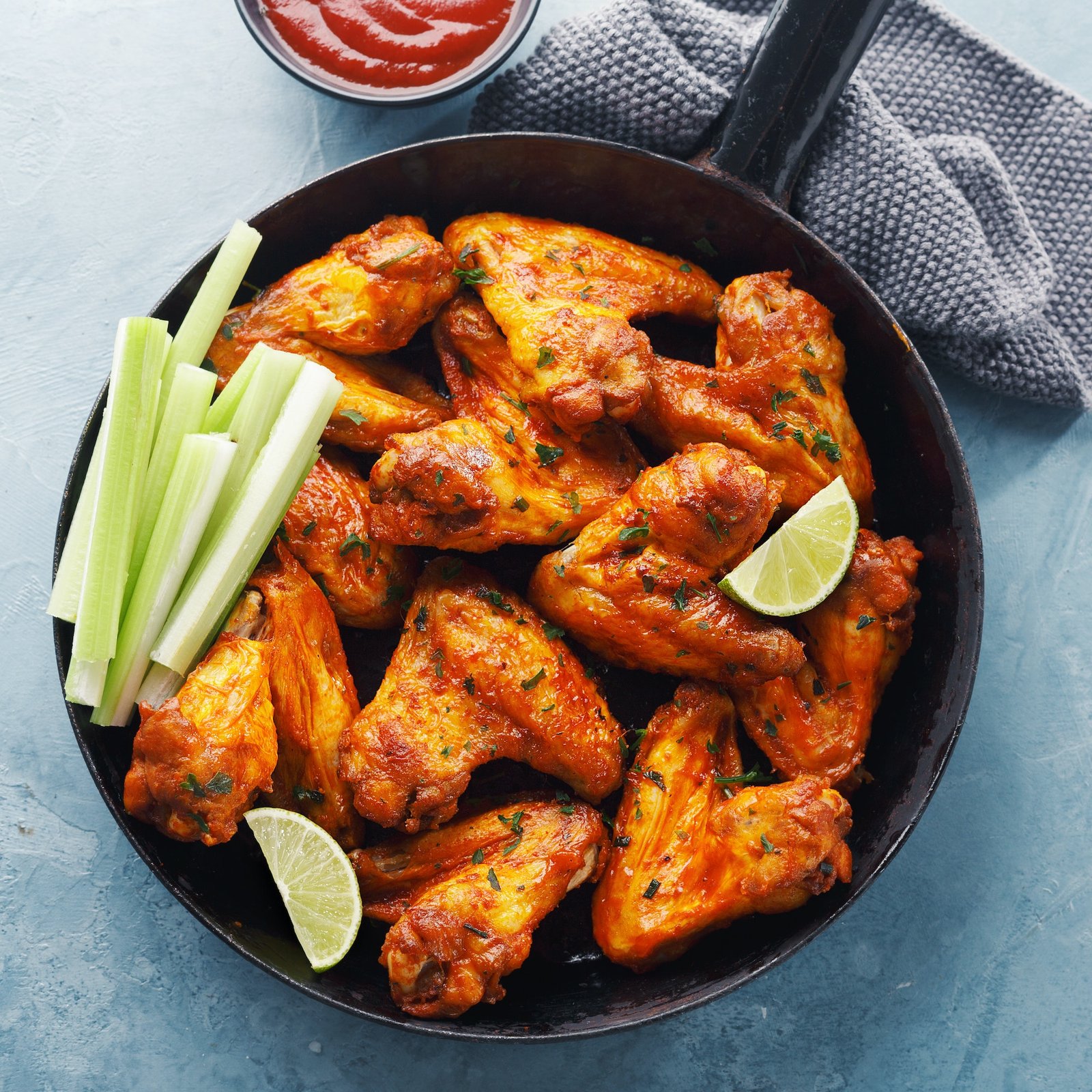 Buffalo chicken wings with celery and lime served in a frying pan